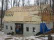 Two rows of sheathing were added to strengthen the trusses. I was unable to get help for the sheathing so I placed it myself. On the side sheathing I started with blocks to hold the placed sheathing while I nailed it. After the first row I used Simpson H clips to hold the sheet in along with a wood clamp.  It was suggested that I place a gable end on the building to stop the roof from behaving like a wing and flying away. Roof sheathing stopped and efforts were directed toward the gable end. 